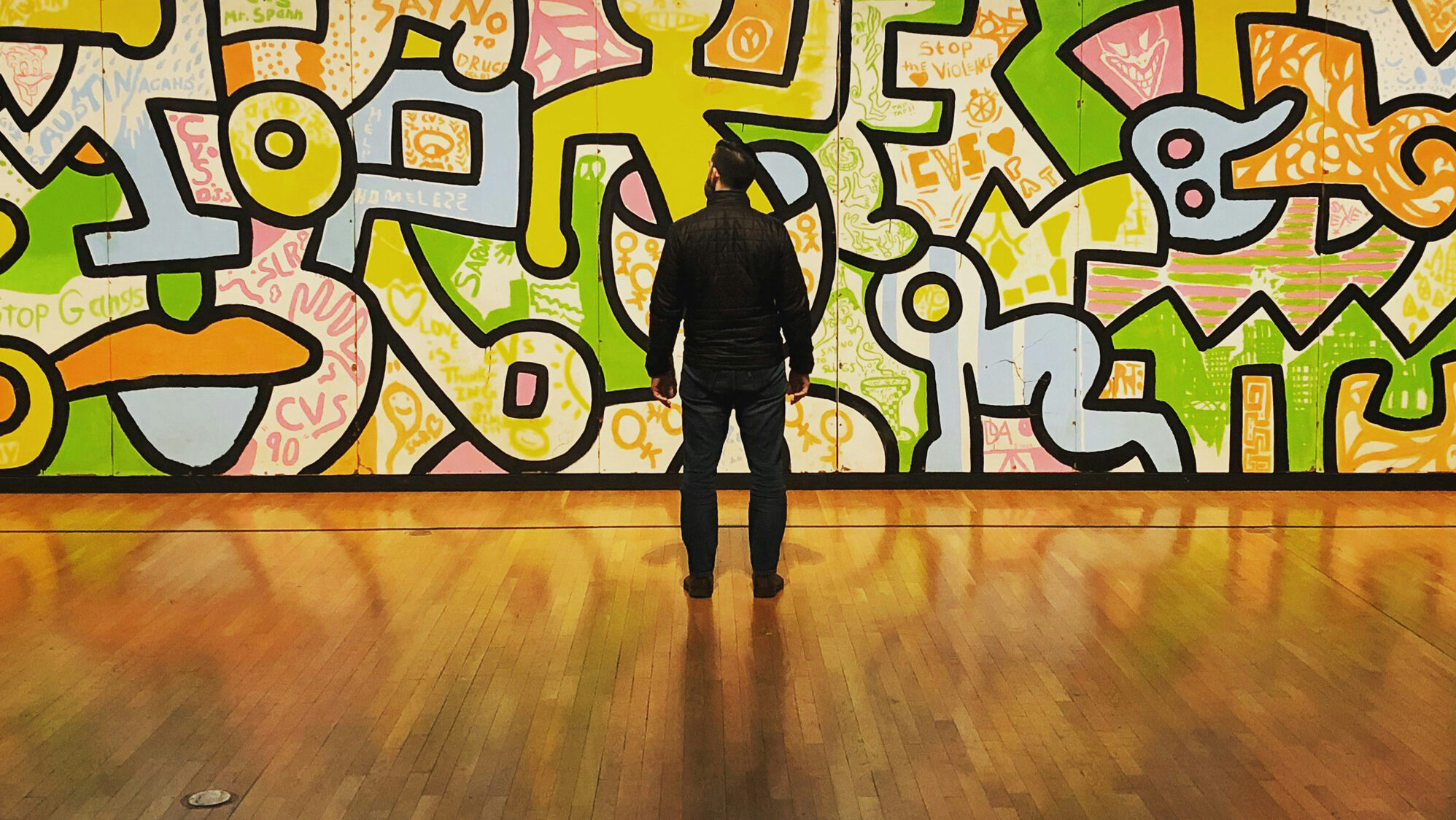 Wide shot of a man from behind looking at an illustrated, bright colored mural