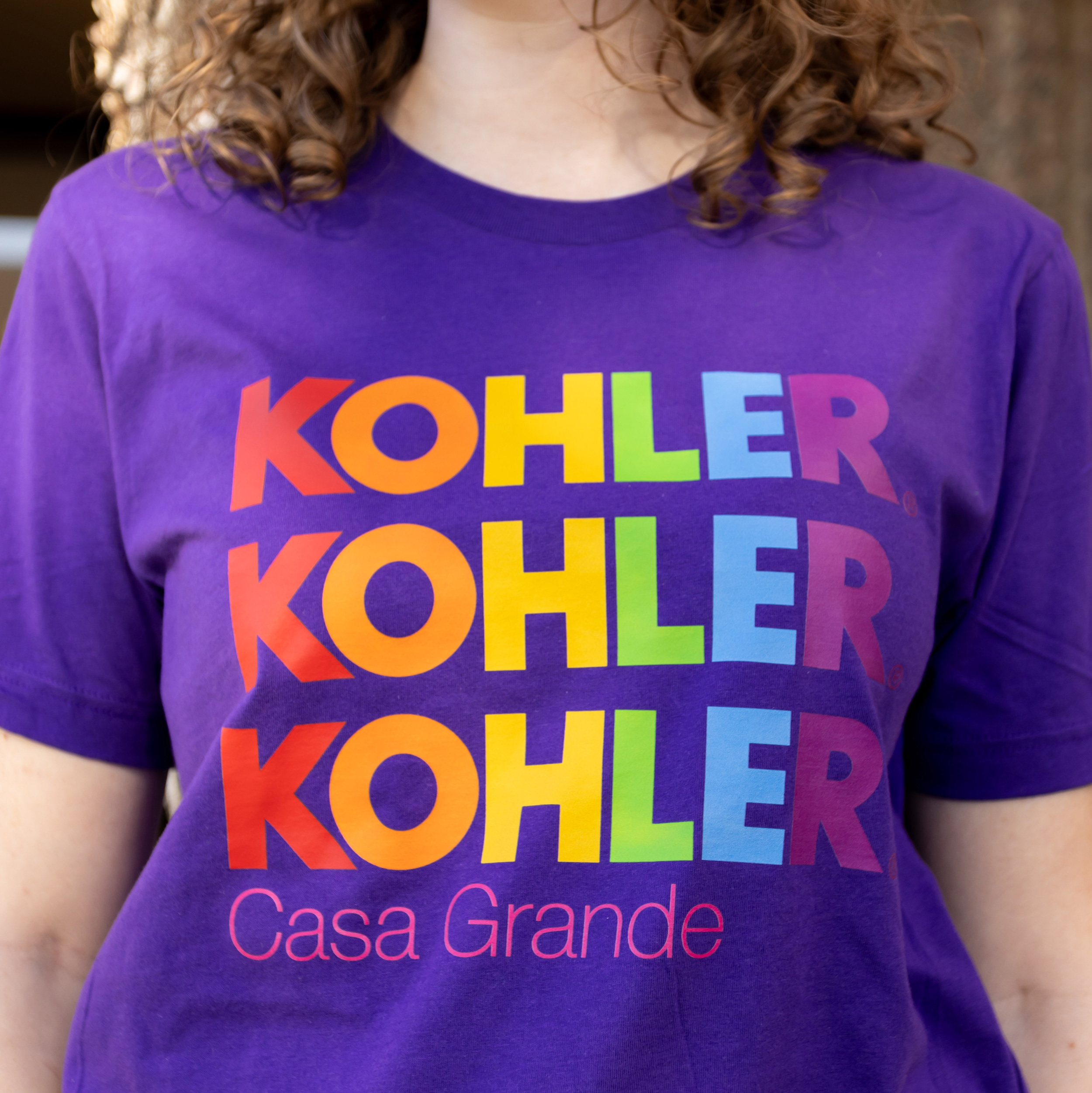 Purple Kohler Casa Grande shirt with the logo in rainbow colors stacked three times