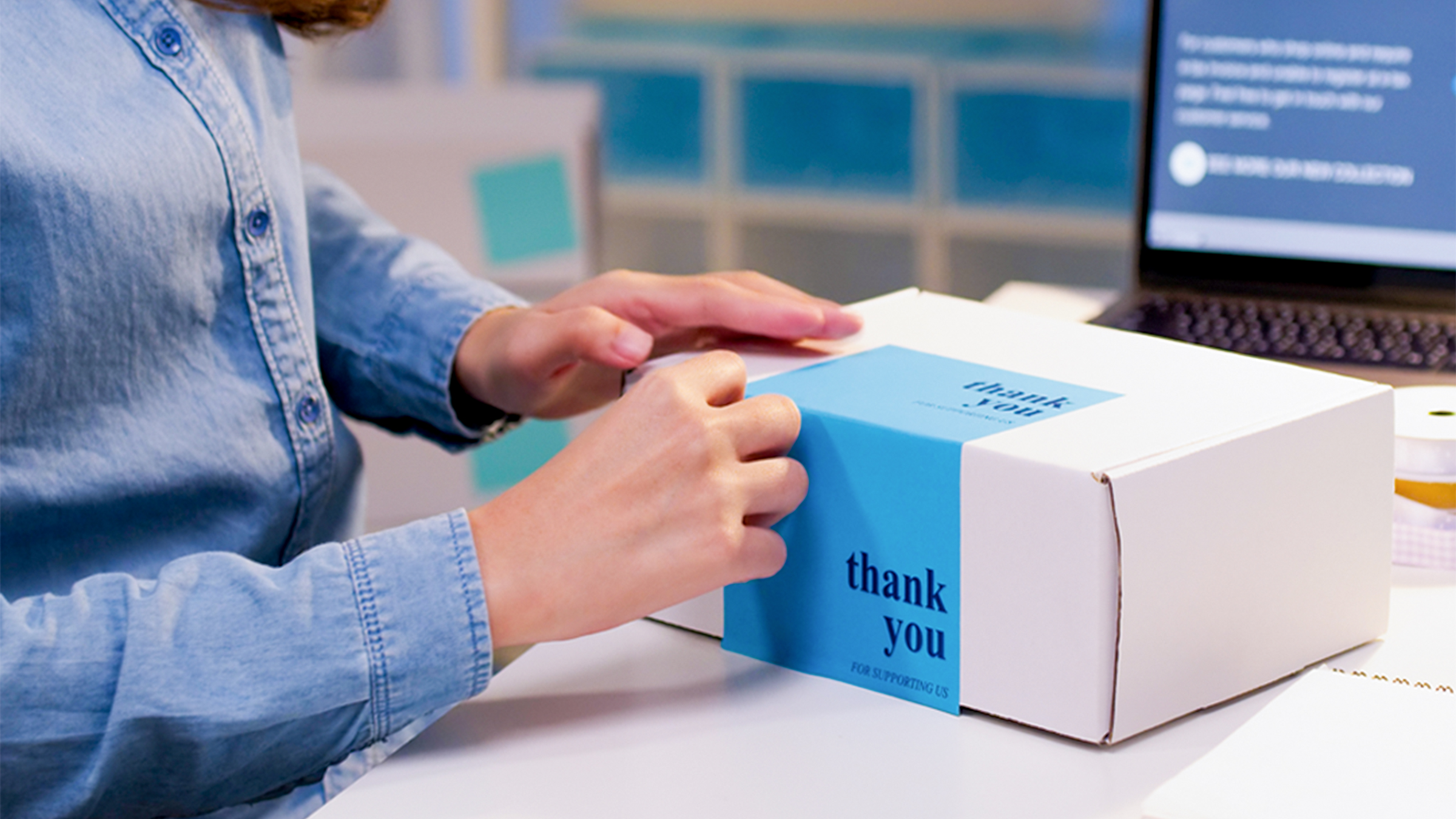 Person at a desk adhering a blue Thank You label to a white box