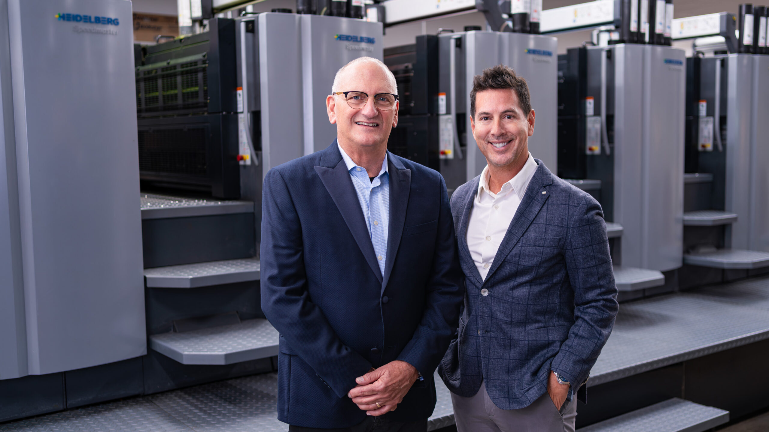 Simon Beltran and Anthony Narducci standing side-by-side in front of a printing press